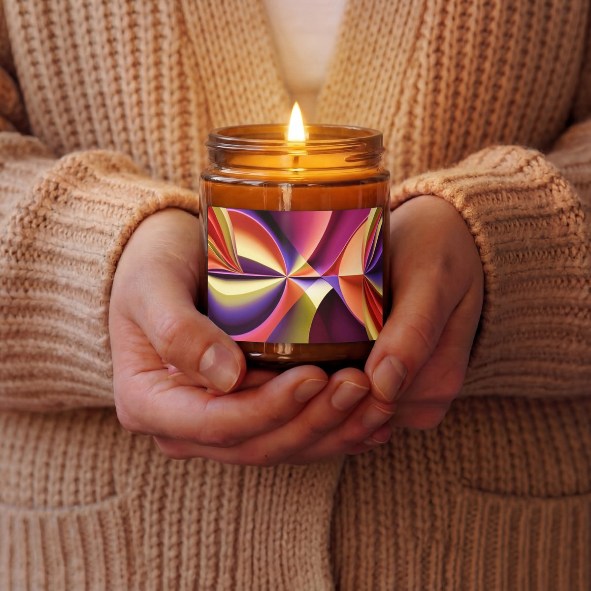 Hands holding a lit Story of Colour scented soy candle in an amber jar with ruby, gold and violet abstract artwork.